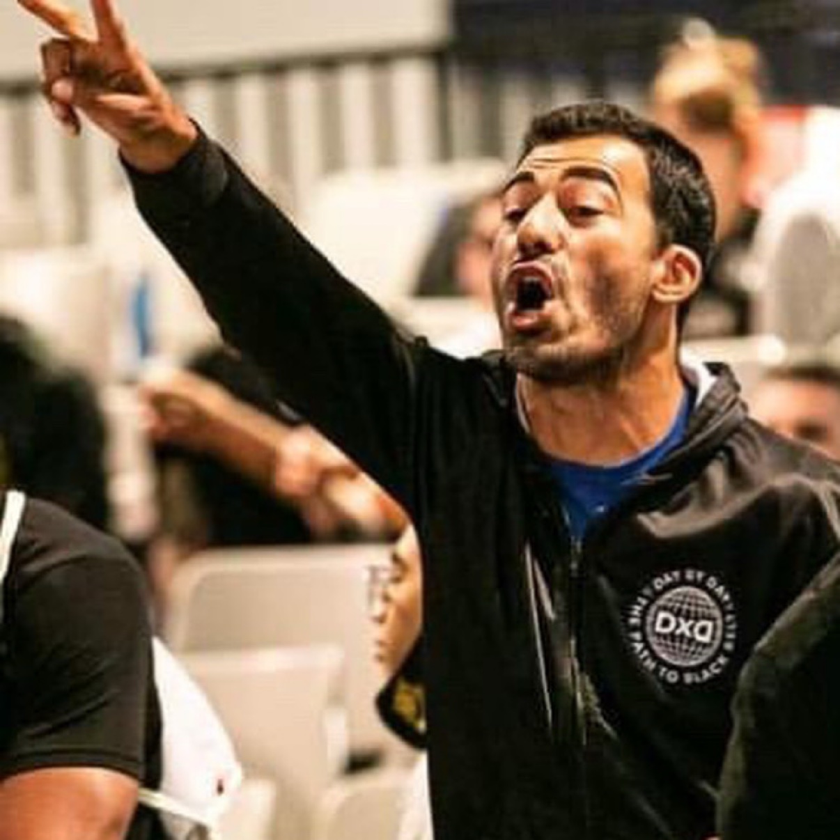 Deivid Dias coaching passionately in a black DxD hoodie with one arm raised