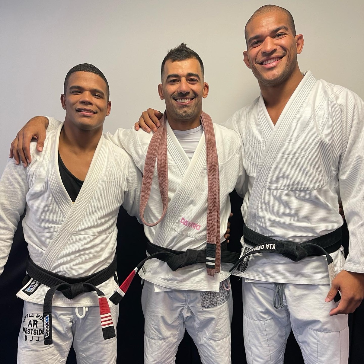 Deivid Dias between two fellow black belts, all wearing white gis