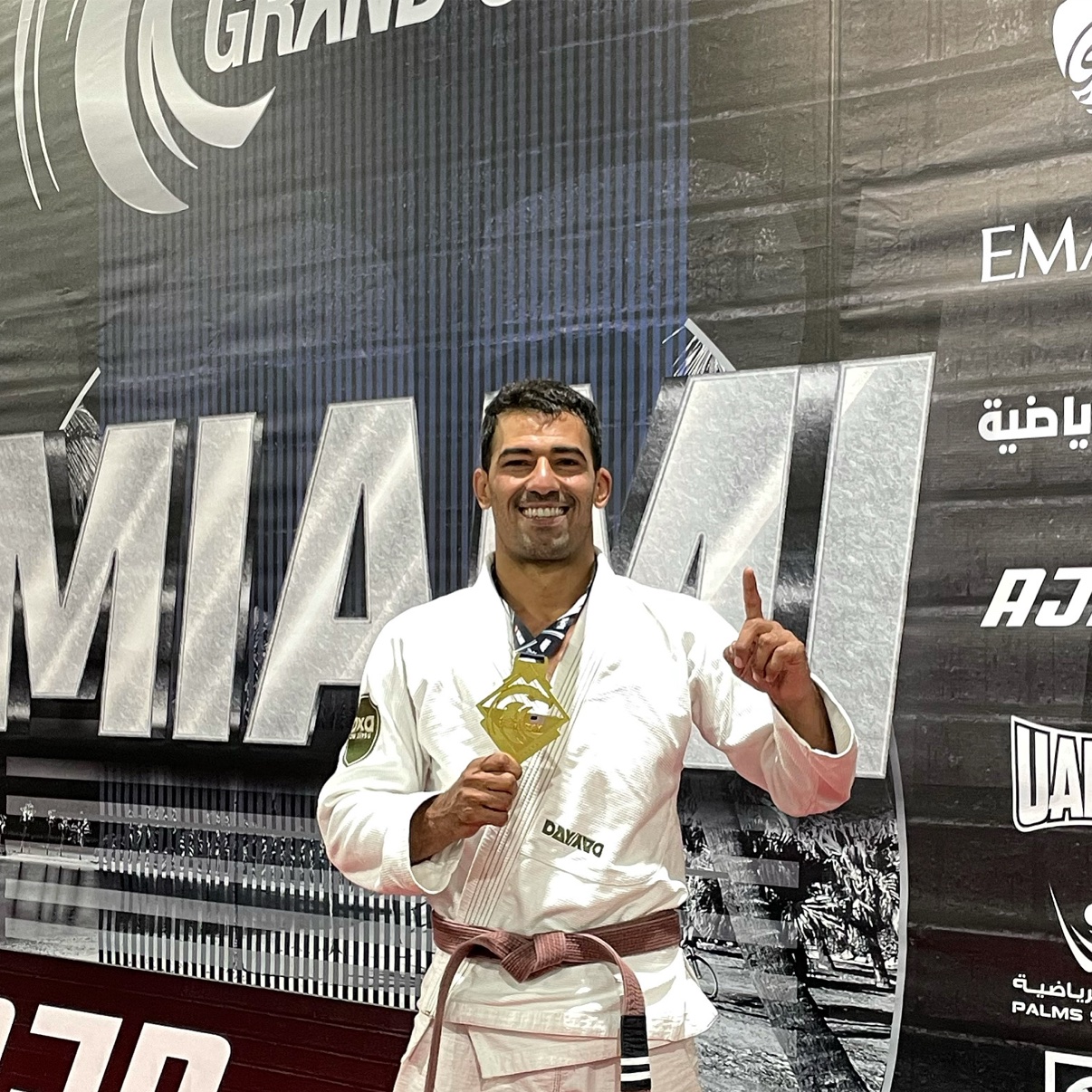 Deivid Dias holding an AJP Miami Grand Slam gold medal in a white gi