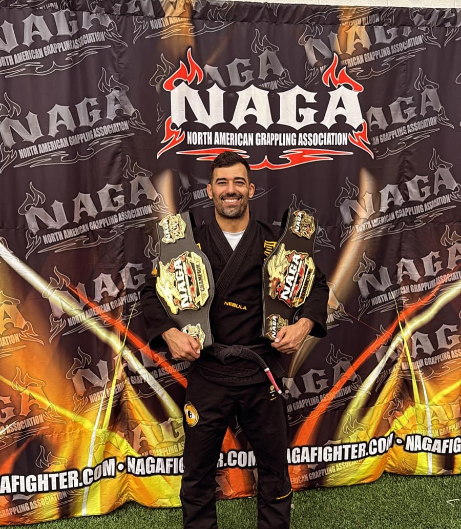 Deivid Dias holding two NAGA championship belts wearing a black Nebula gi